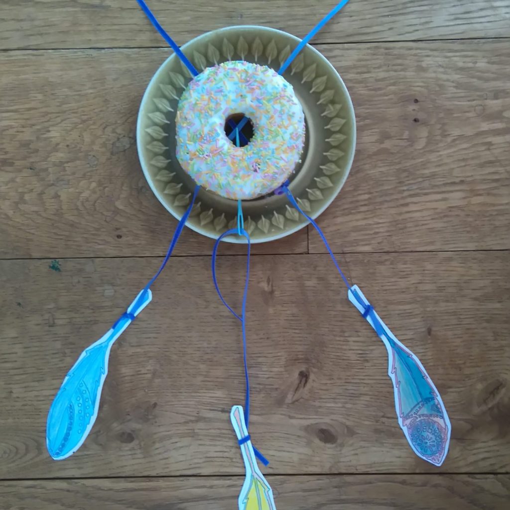 doughnut with ribbons threaded through and feathers hanging from it