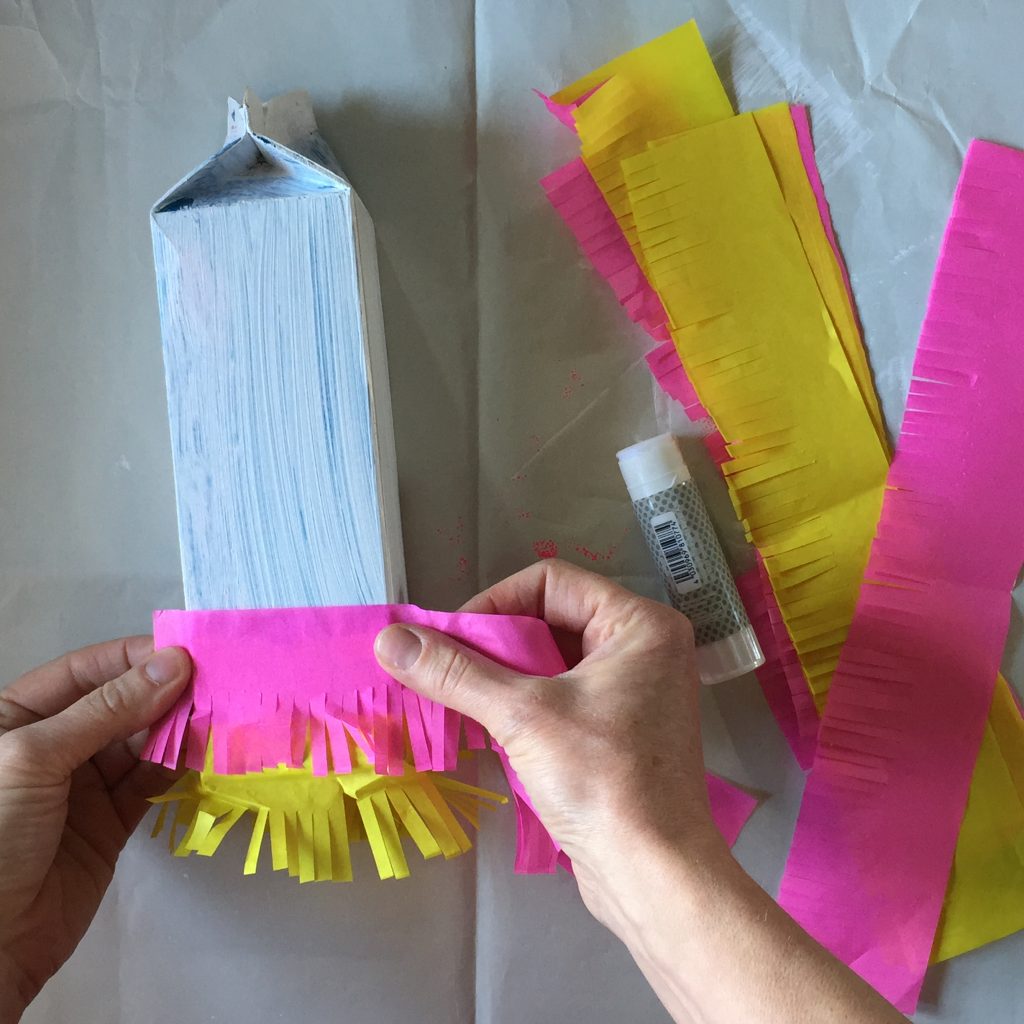 sticking homemade fringing onto a sustainable party crafts milk carton pinata