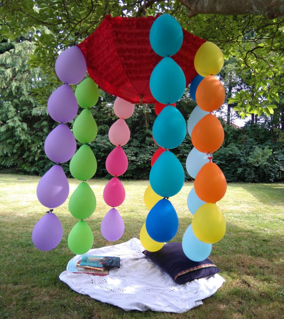 umbrella hanging in a tree with colourful compostable balloons trailing from it