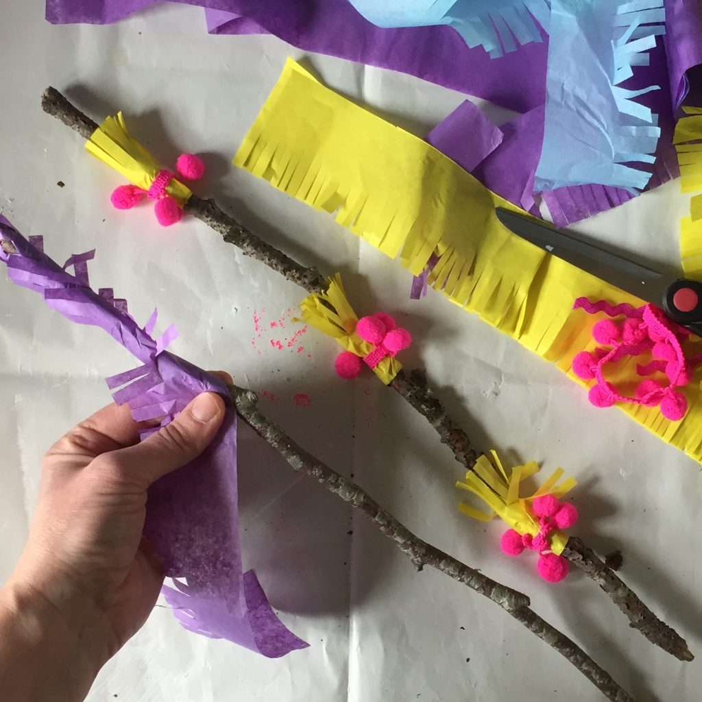 sticks from nature being decorated with tissue paper and ribbon for sustainable party pinata crafts