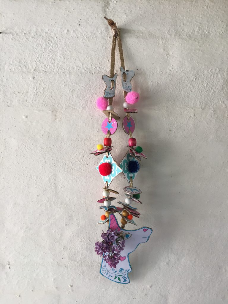 a pretty kids unicorn cardboard junk necklace with flowers, pompoms and sequins made with a free childrens craft printable