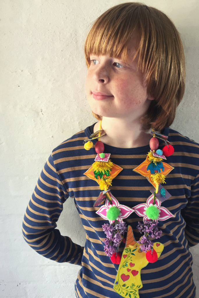 a boy wearing a homemade recycled cardboard junk necklace with flowers and unicorns