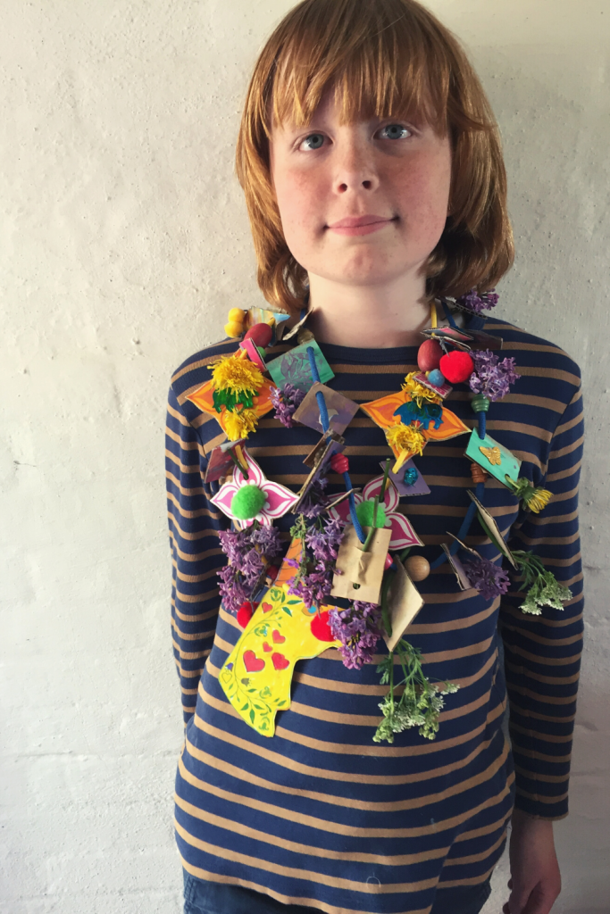 boy wearing a homemade cardboard unicorn necklace with flowers and foliage made with a free craft printable